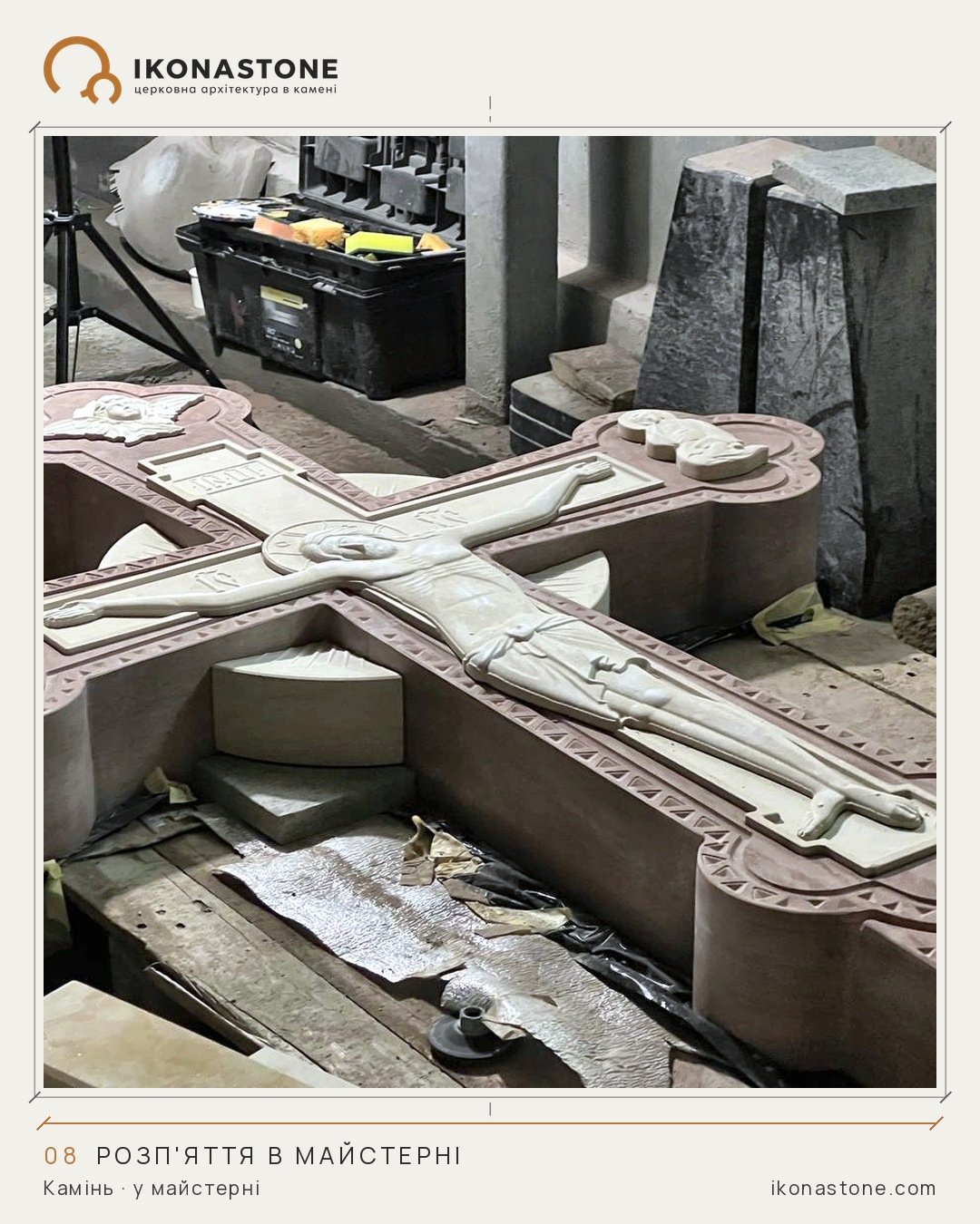 A stone cross lying flat in the workshop: a pale figure of Christ on a darker background, figures in relief at the ends, an ornament along the edge