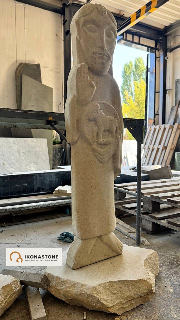 Stone sculpture of Christ the Good Shepherd with a lamb and a raised right hand, in the workshop